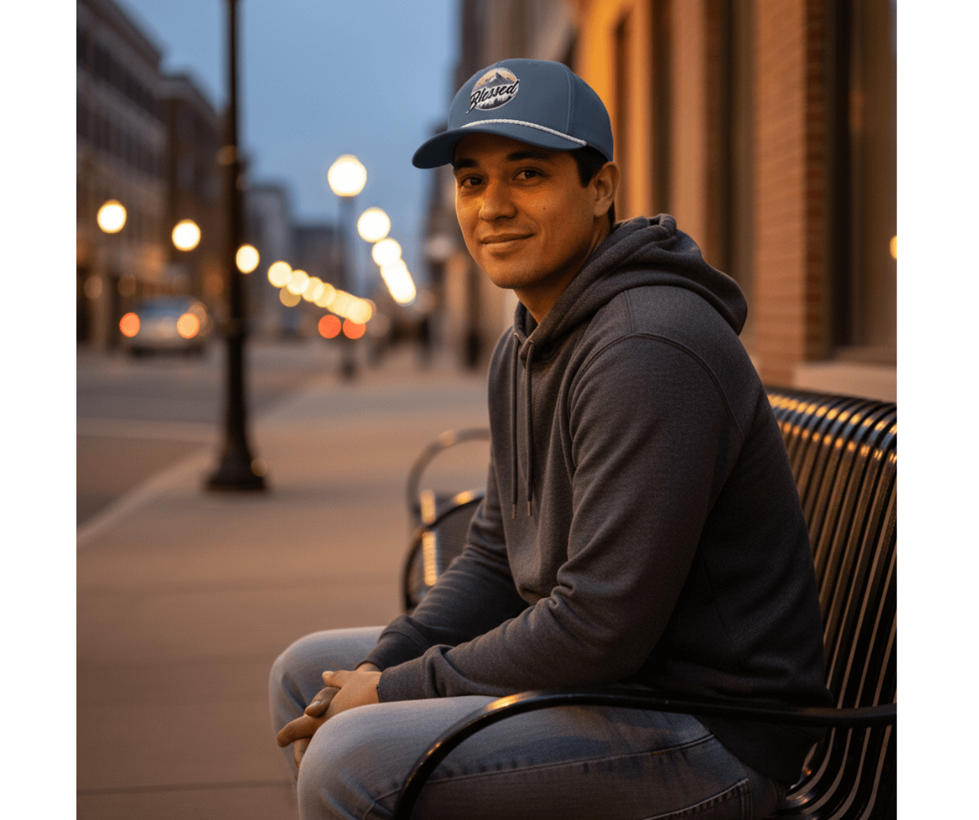 Man sitting on a bench wearing a cap and hoodie with a city street background