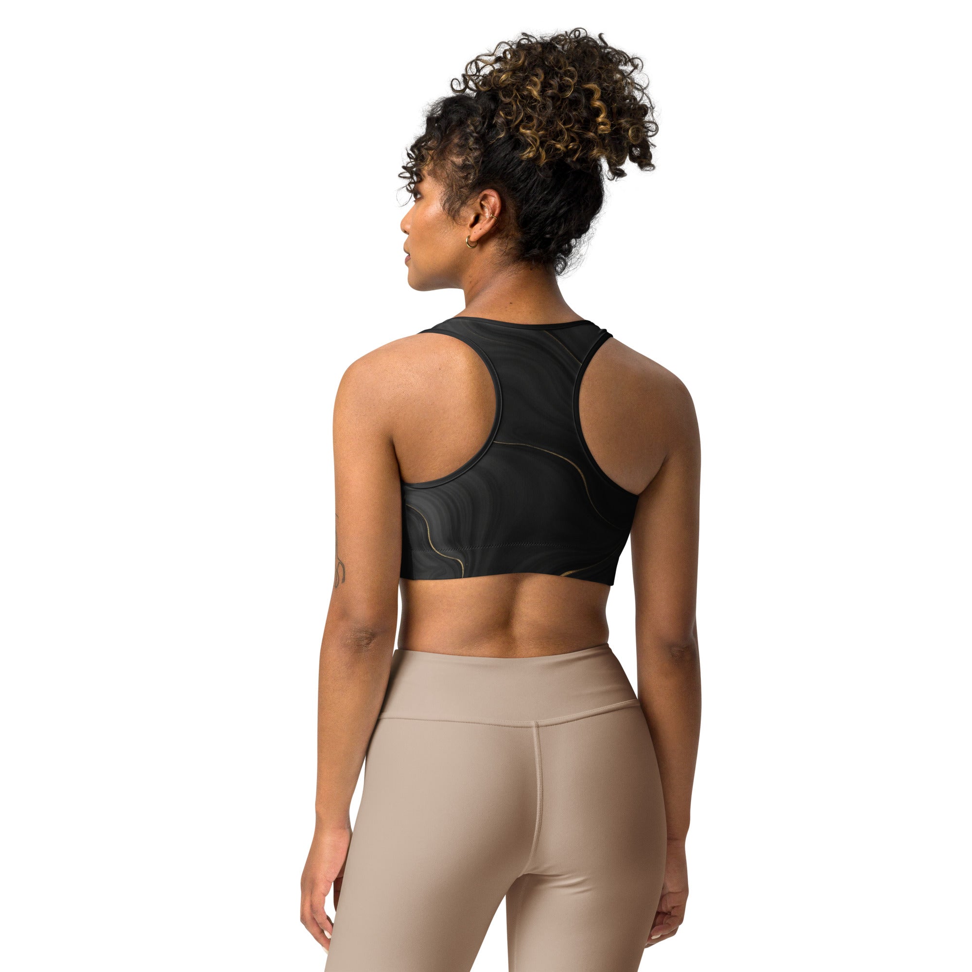 Woman wearing a black sports bra and beige leggings on a white background